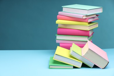 Stack of colorful books on light blue background, space for text