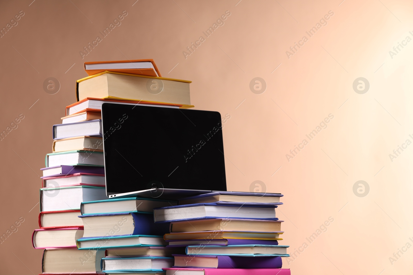 Photo of Stacks of colorful books and laptop on light brown background, space for text