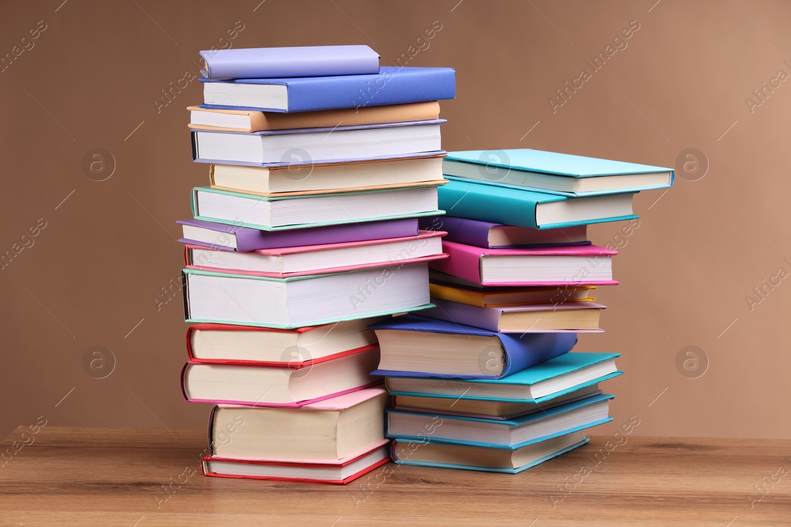 Photo of Stacks of colorful books on wooden table against light brown background