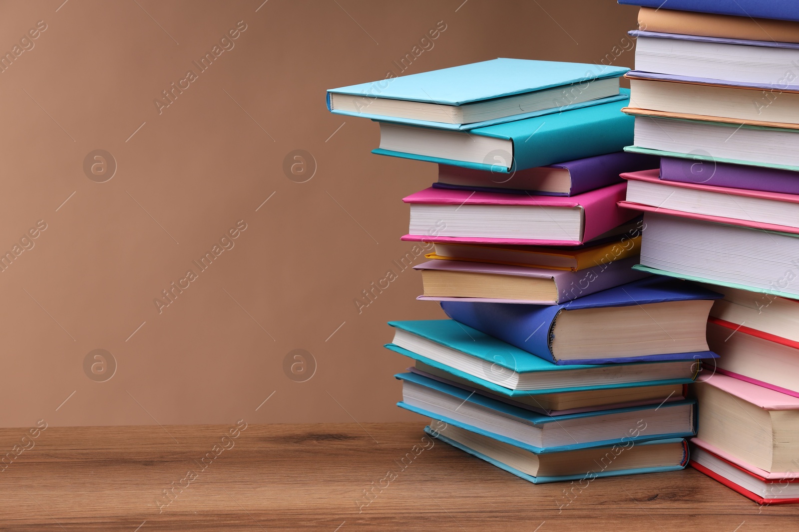 Photo of Stacks of colorful books on wooden table against light brown background, space for text