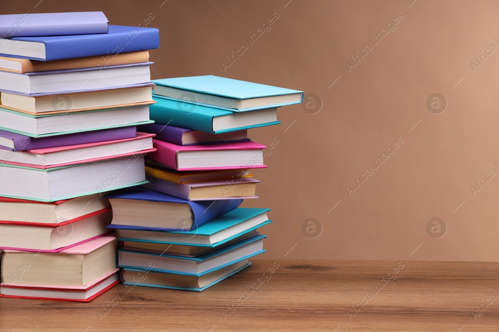 Photo of Stacks of colorful books on wooden table against light brown background, space for text