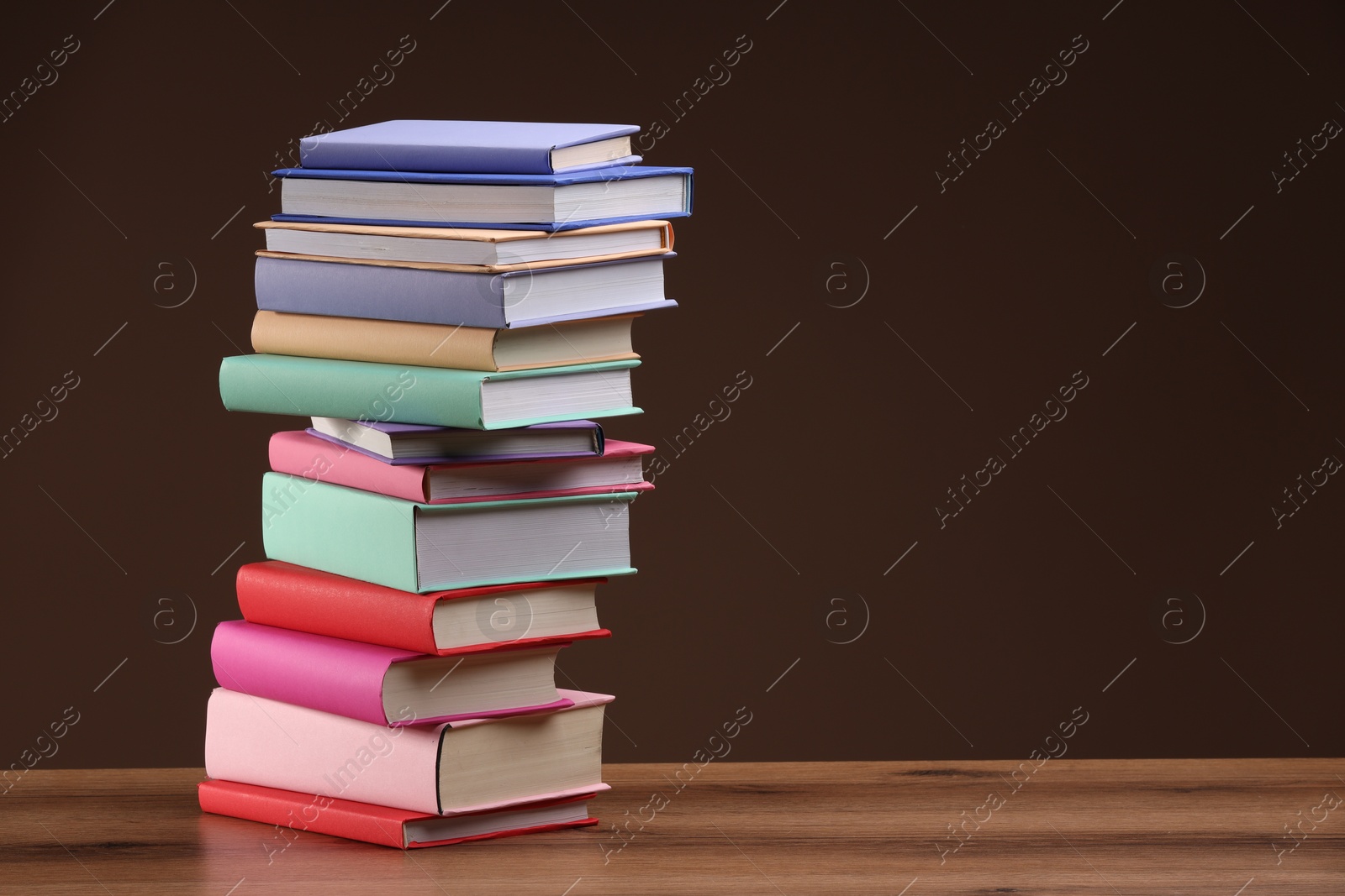 Photo of Stack of colorful books on wooden table against light brown background, space for text