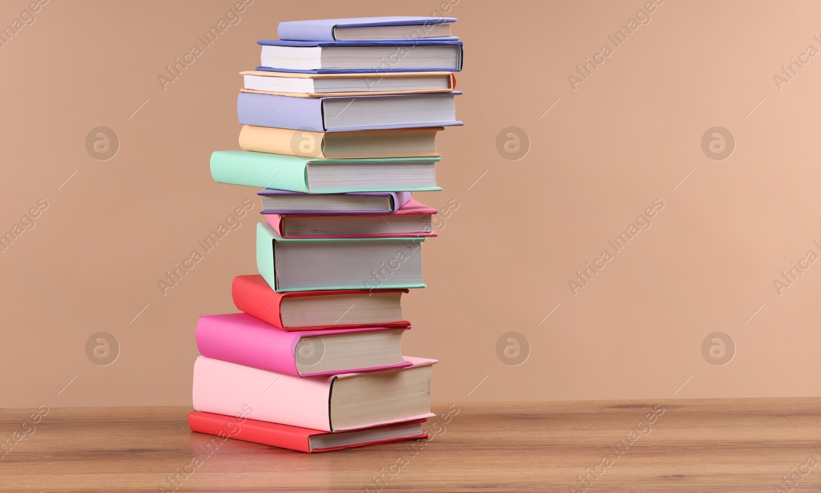 Photo of Stack of colorful books on wooden table against light brown background, space for text