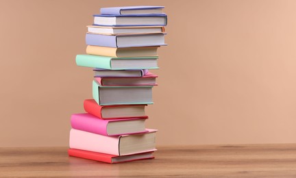 Photo of Stack of colorful books on wooden table against light brown background, space for text