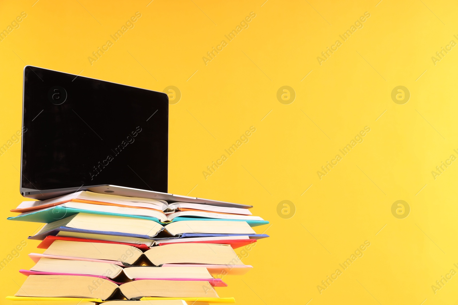 Photo of Stack of colorful books and laptop on yellow background, space for text