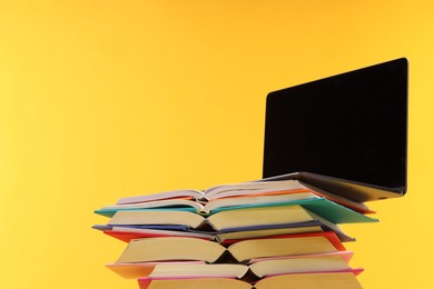 Stack of colorful books and laptop on yellow background, space for text