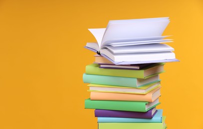 Stack of colorful books on orange background, space for text