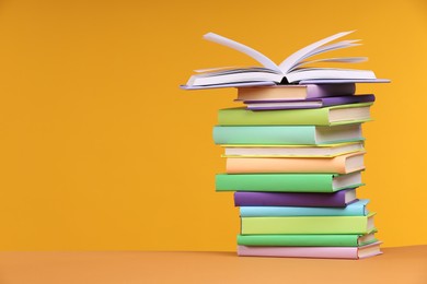 Photo of Stack of colorful books on orange background, space for text