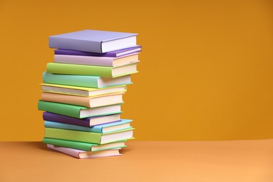 Photo of Stack of colorful books on orange background, space for text