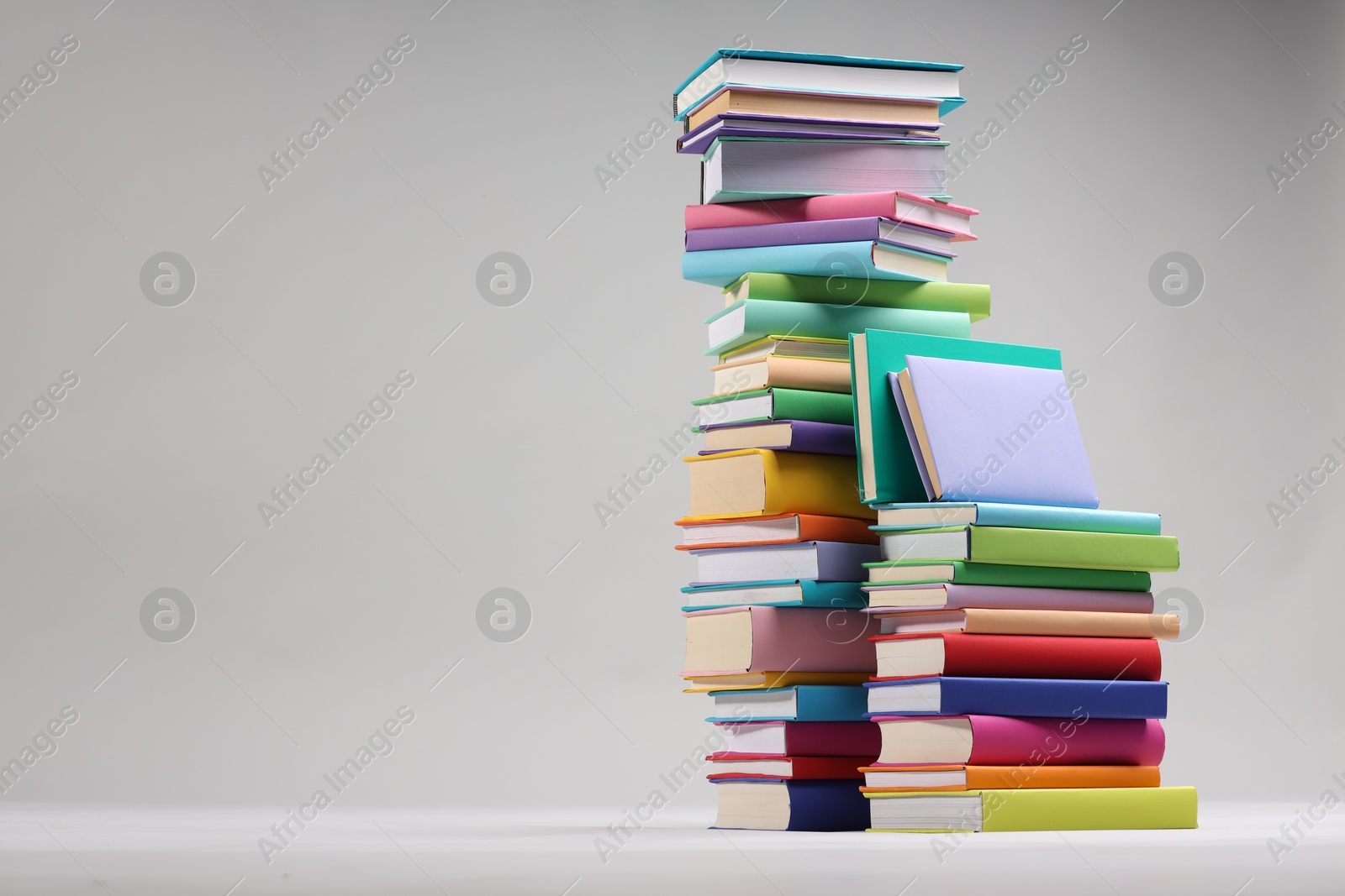 Photo of Stacks of colorful books on light grey background, space for text