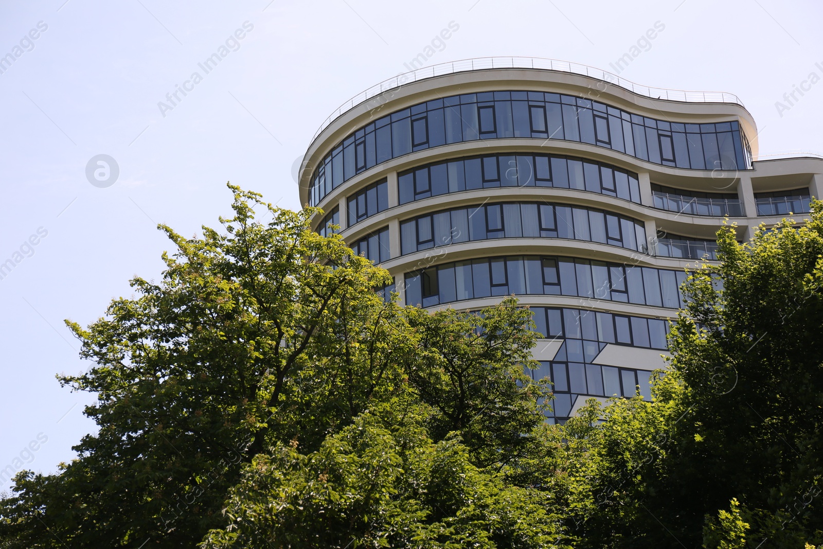 Photo of Modern building with glass windows and green trees outdoors, low angle view