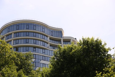 Modern building with glass windows and green trees outdoors, low angle view