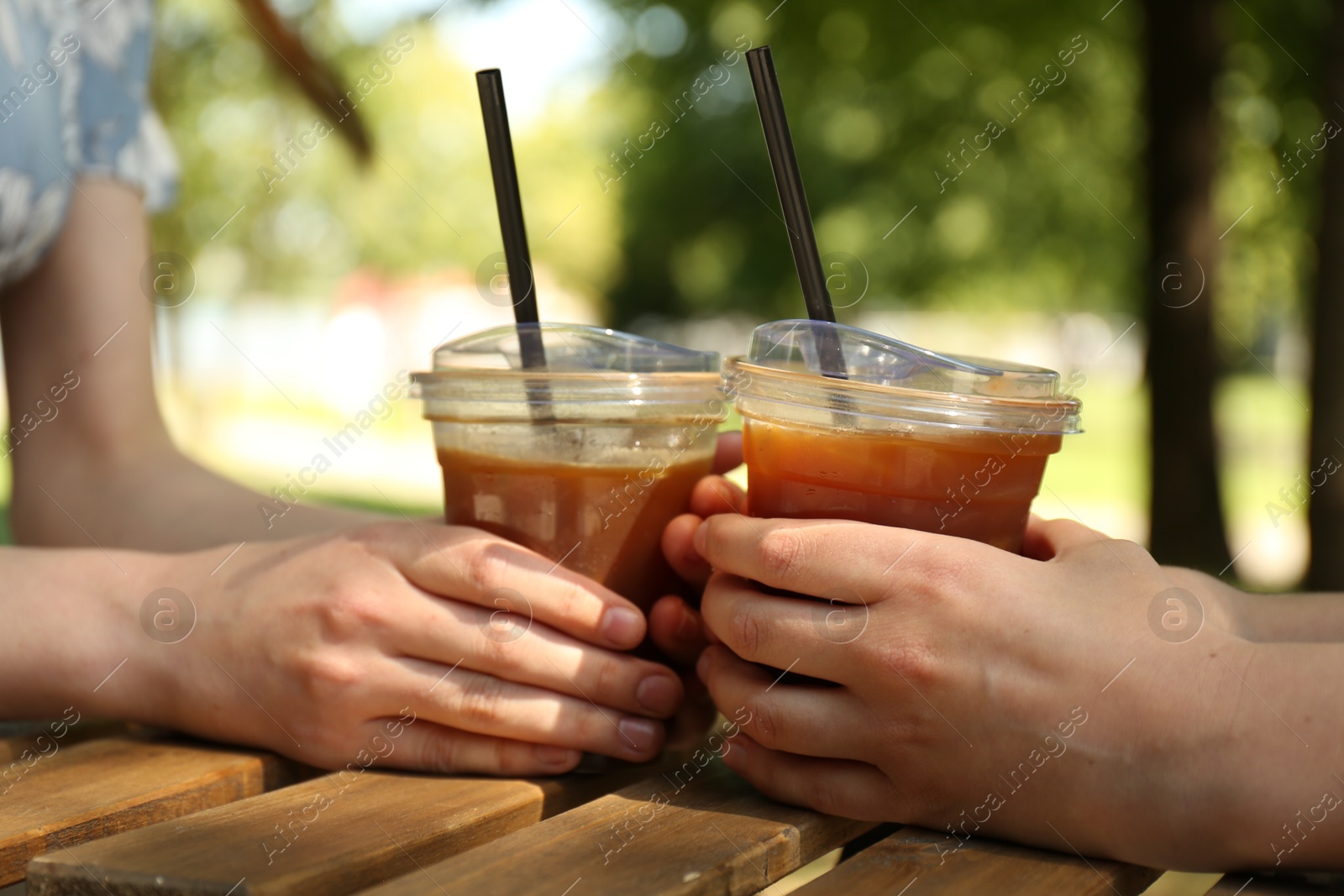Photo of Women with tasty refreshing drinks at wooden table outdoors, closeup