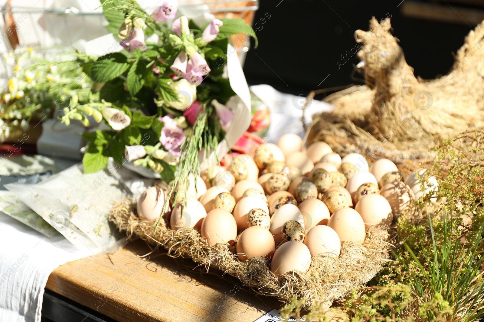 Photo of Quail and chicken eggs in container with straw on wooden table outdoors, closeup