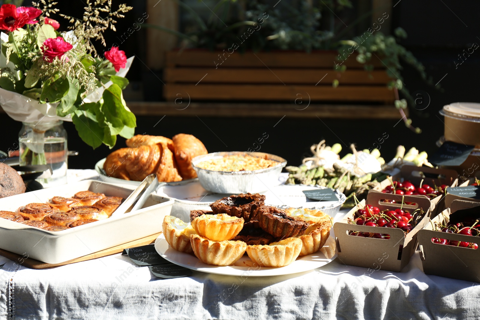 Photo of Tasty fresh pastries, red ripe cherries and other products on table outdoors