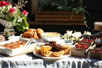 Tasty fresh pastries, red ripe cherries and other products on table outdoors