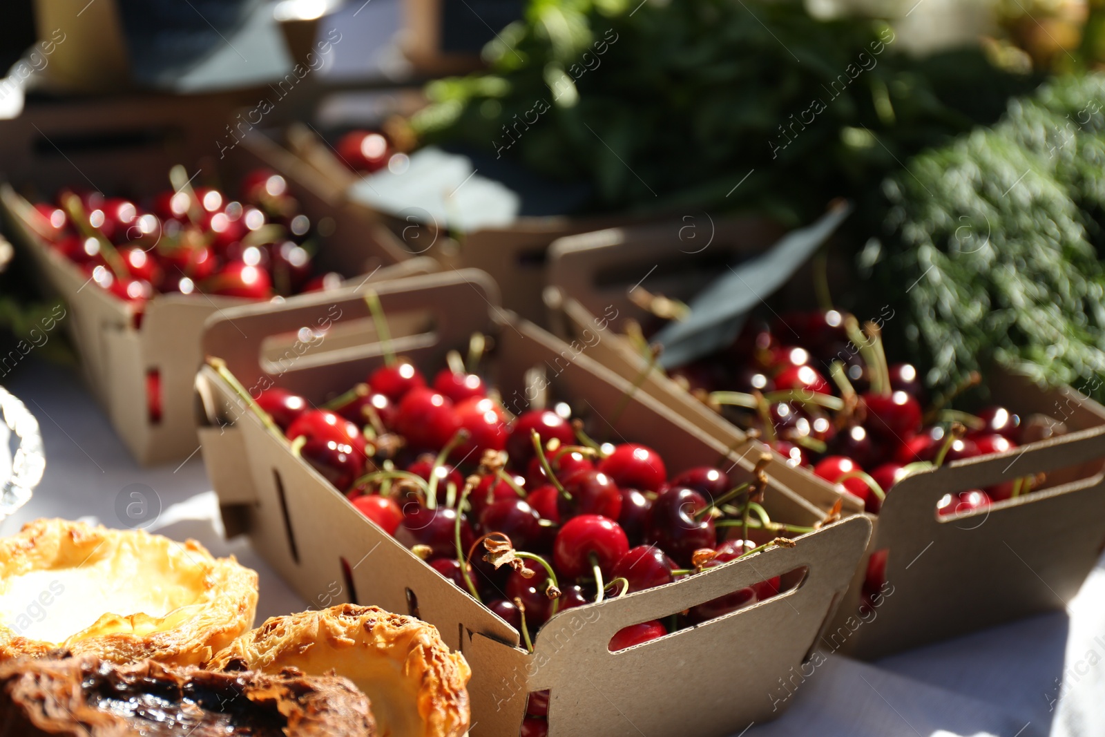 Photo of Tasty ripe red cherries in cardboard boxes on table outdoors, closeup