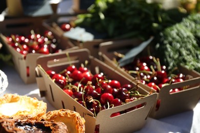 Photo of Tasty ripe red cherries in cardboard boxes on table outdoors, closeup