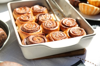 Photo of Tasty cinnamon rolls in baking dish on table outdoors, closeup