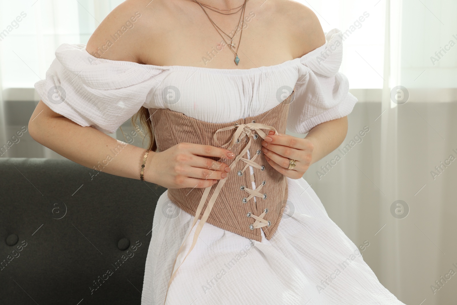 Photo of Woman in stylish corset sitting on sofa indoors, closeup