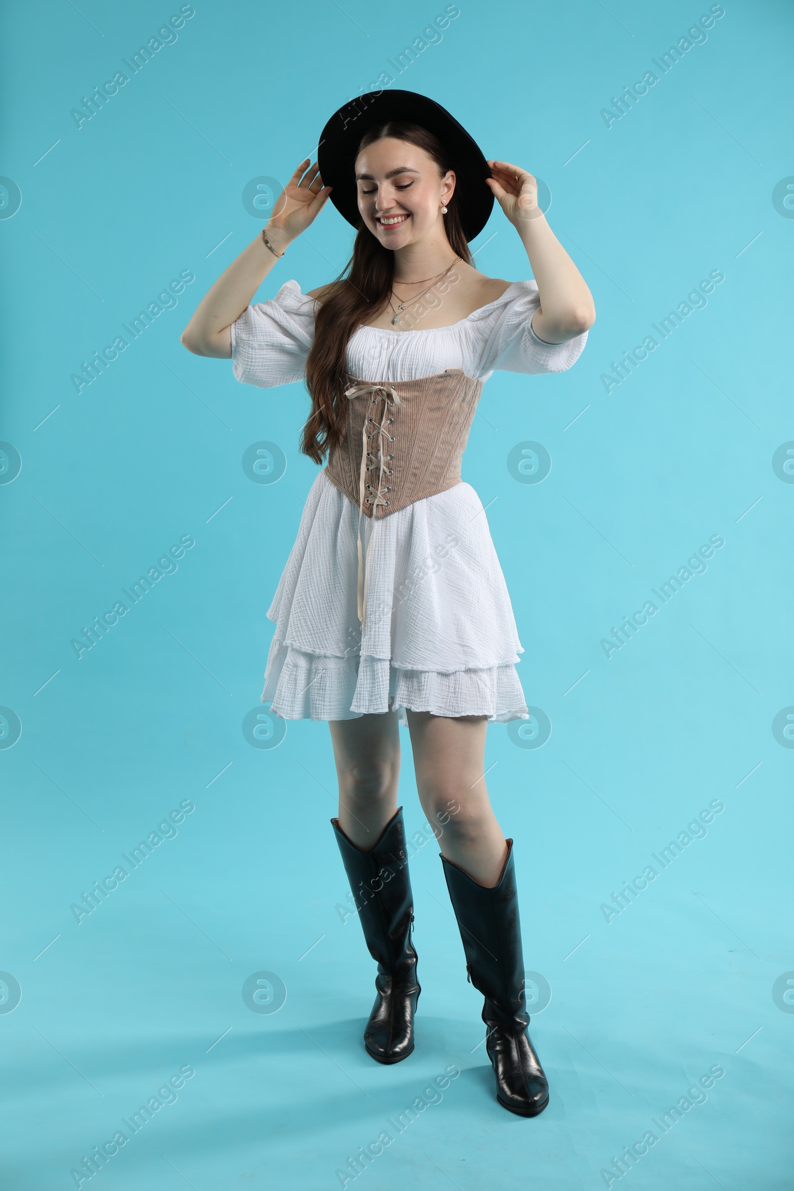 Photo of Smiling woman in velvet corset and hat on light blue background