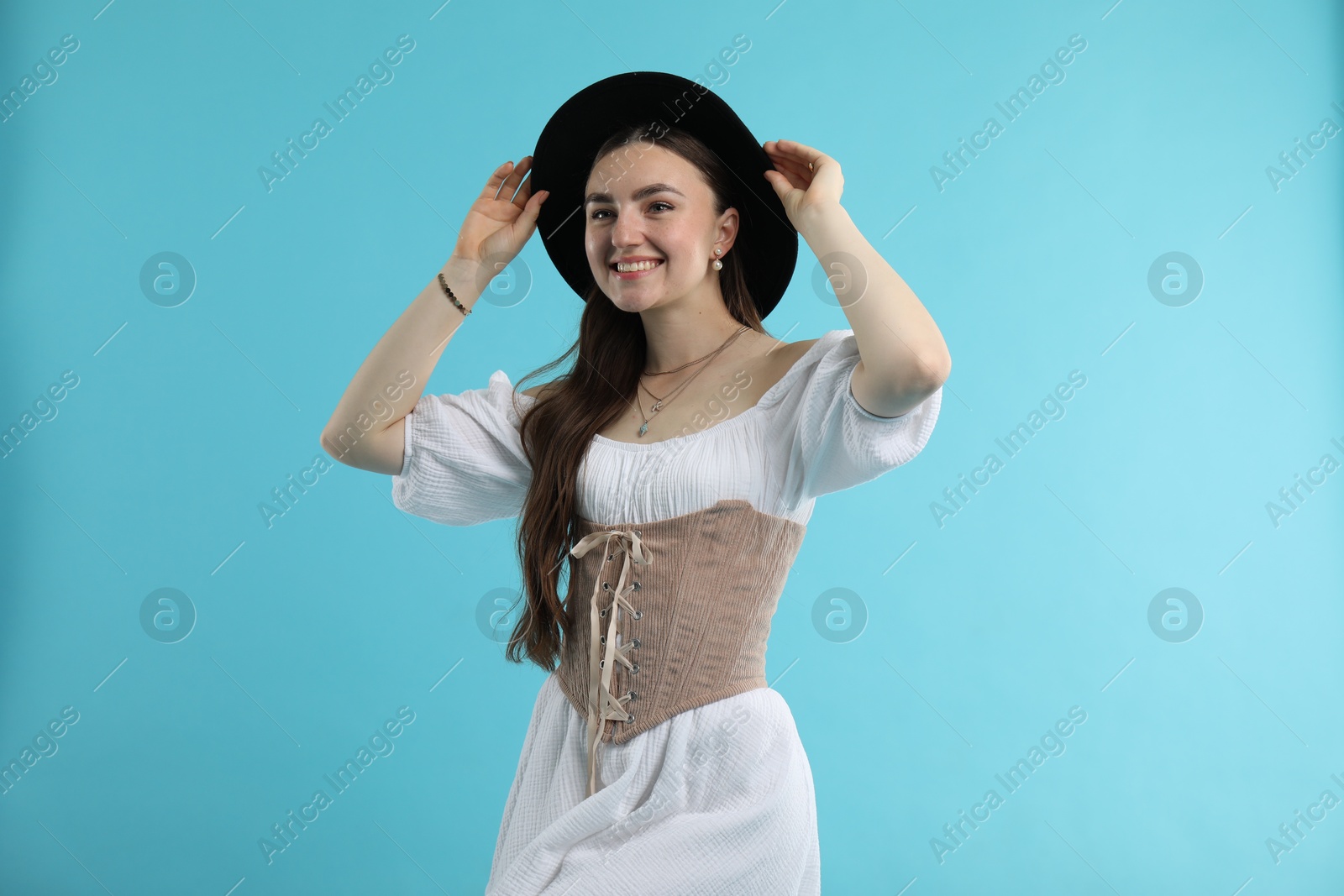 Photo of Smiling woman in velvet corset and hat posing on light blue background