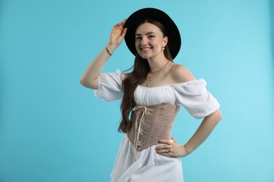 Smiling woman in velvet corset and hat posing on light blue background