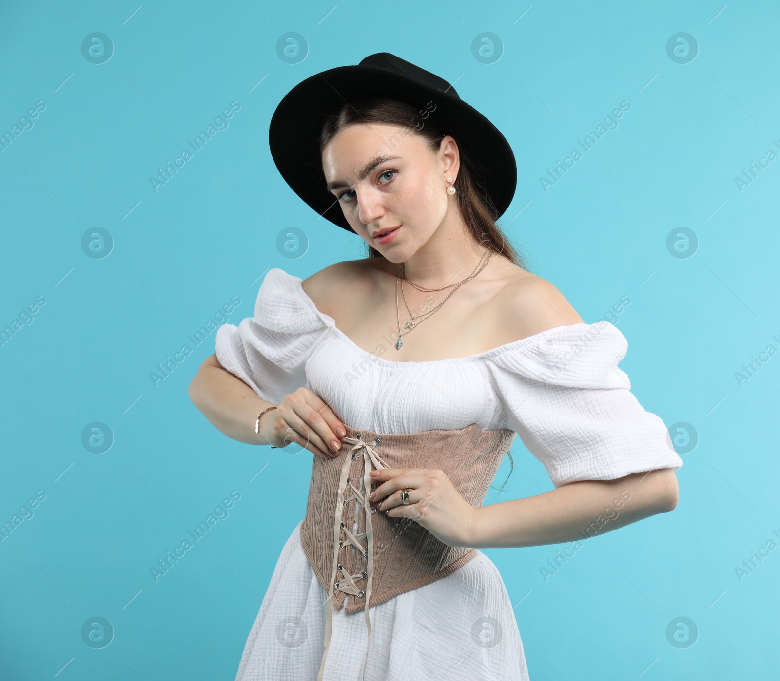 Photo of Beautiful woman in velvet corset and hat posing on light blue background. Space for text