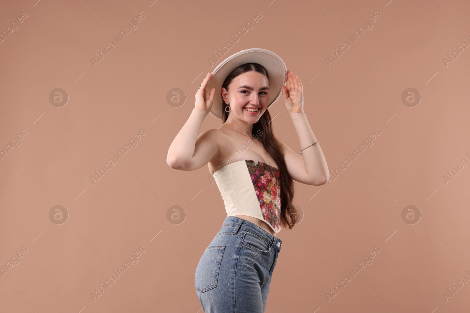 Photo of Smiling woman in stylish corset and hat posing on beige background