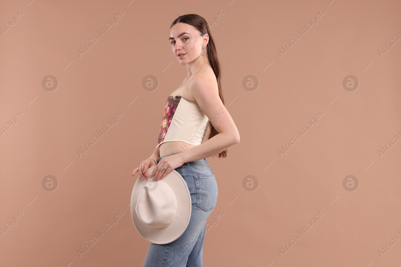 Photo of Beautiful woman in stylish corset with hat posing on beige background