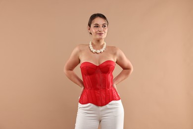 Photo of Beautiful woman in red corset posing on beige background
