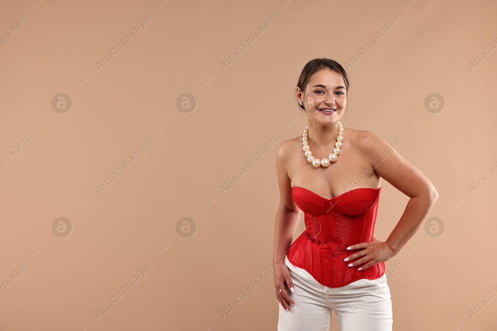 Photo of Smiling woman in red corset posing on beige background. Space for text