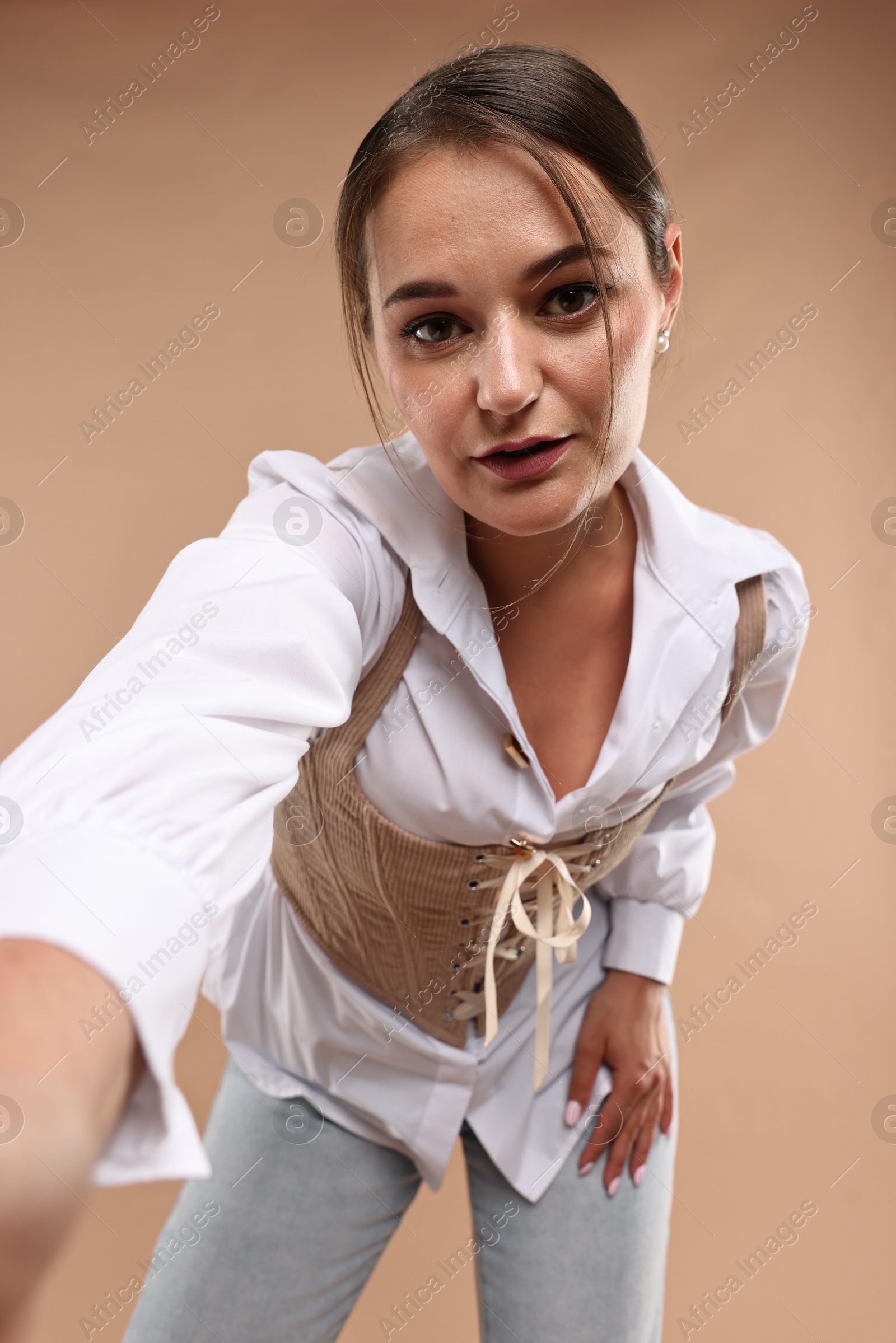 Photo of Beautiful woman in stylish corset taking selfie on beige background