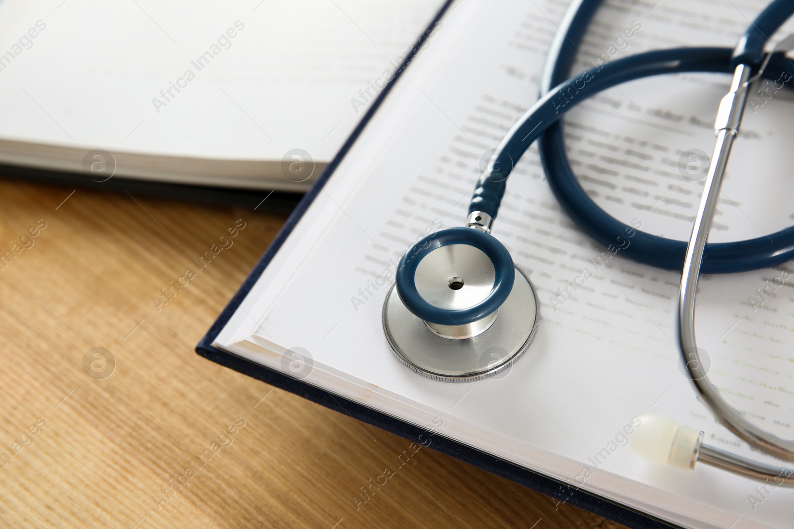 Photo of One new medical stethoscope and books on wooden table, closeup