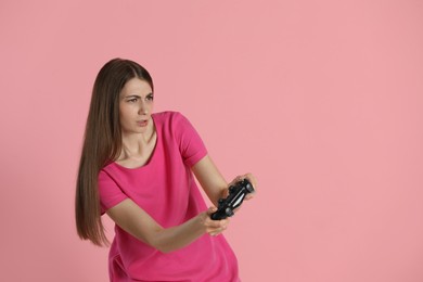 Woman playing video games with controller on pink background, space for text