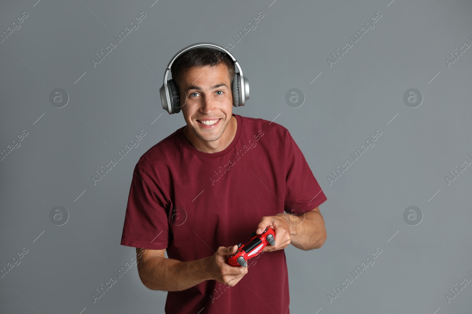 Photo of Happy man in headphones playing video games with controller on gray background