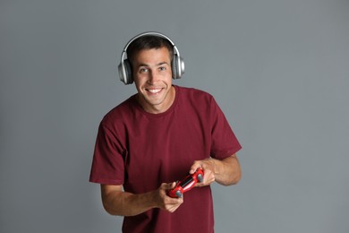 Photo of Happy man in headphones playing video games with controller on gray background