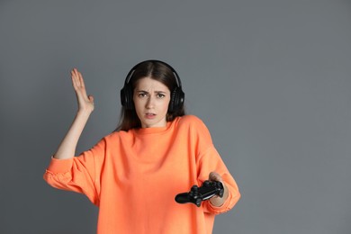 Woman in headphones with controller on gray background, space for text