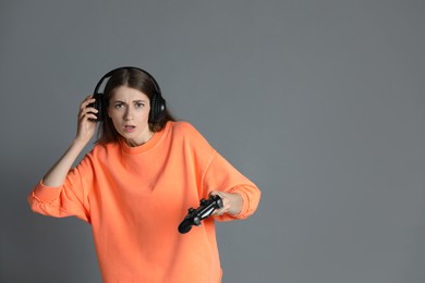 Photo of Woman in headphones playing video games with controller on gray background, space for text