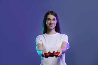 Happy woman playing video games with controller on violet background