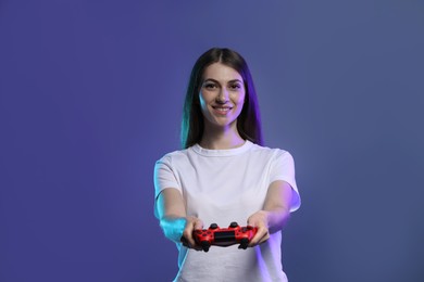 Photo of Happy woman playing video games with controller on violet background