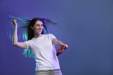 Photo of Happy woman playing video games with controller on violet background, space for text