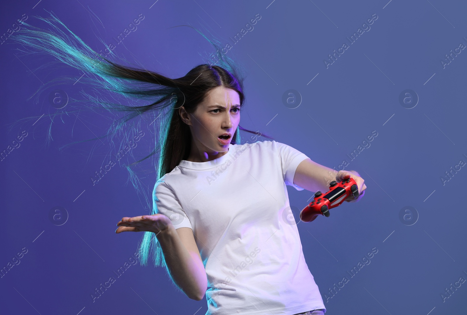 Photo of Surprised woman playing video games with controller on violet background, space for text