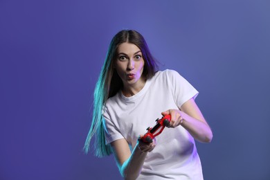 Surprised woman playing video games with controller on violet background