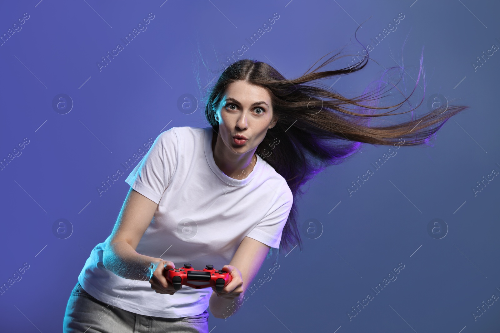 Photo of Surprised woman playing video games with controller on violet background