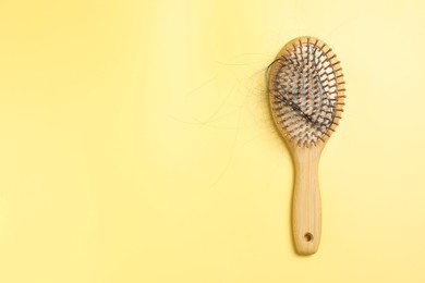 Photo of Wooden brush with lost hair on yellow background, top view. Space for text