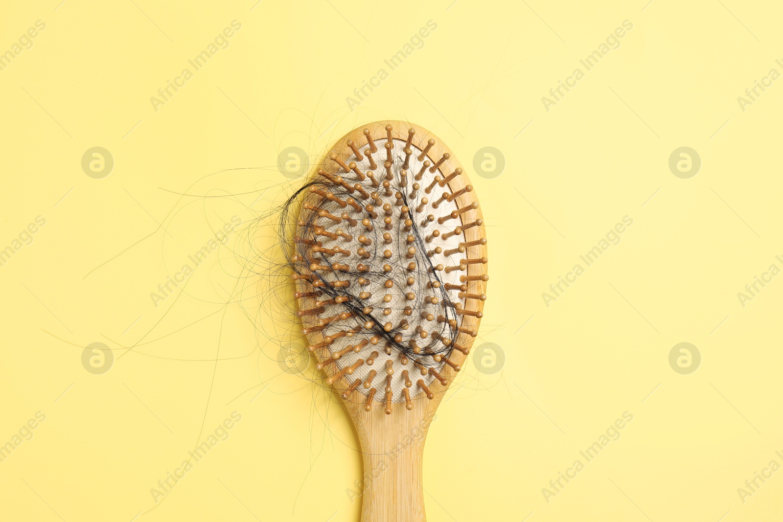 Photo of Wooden brush with lost hair on yellow background, top view