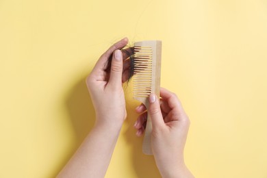 Photo of Woman taking her lost hair from comb on yellow background, top view