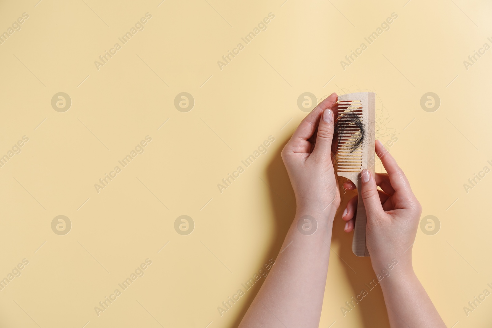 Photo of Woman holding comb with lost hair on yellow background, top view. Space for text