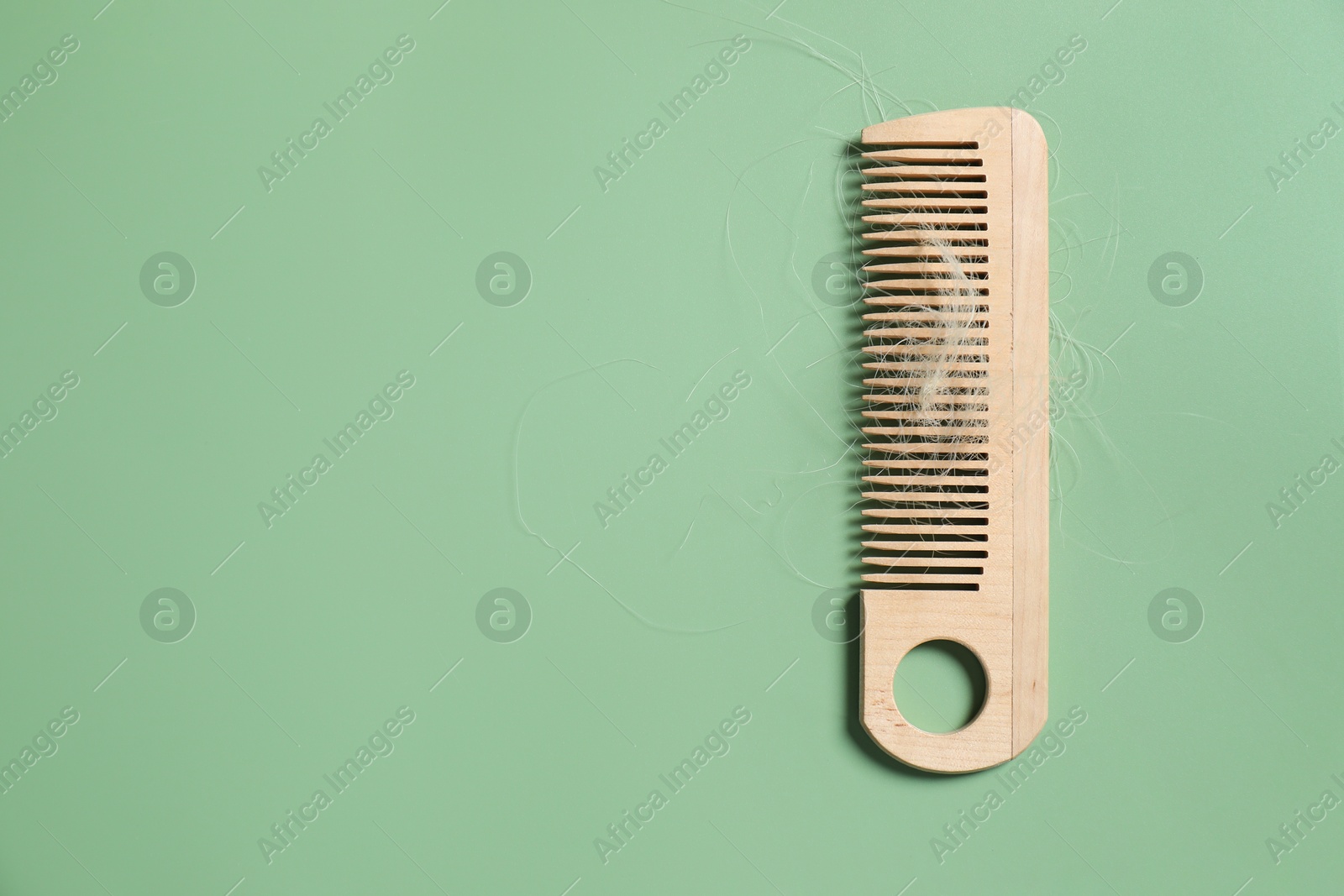 Photo of Wooden comb with lost hair on green background, top view. Space for text